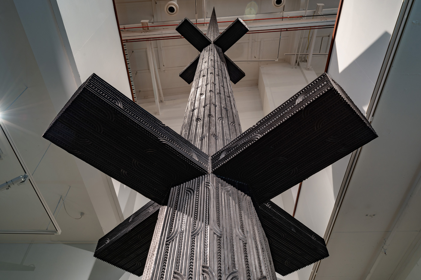 Image of Brett Graham's carved niu pole work titled Cease Tide of Wrongdoing - an intricately carved black kauri work that stands almost 10m tall in the Govett-Brewster Art Gallery, rising to a spike.