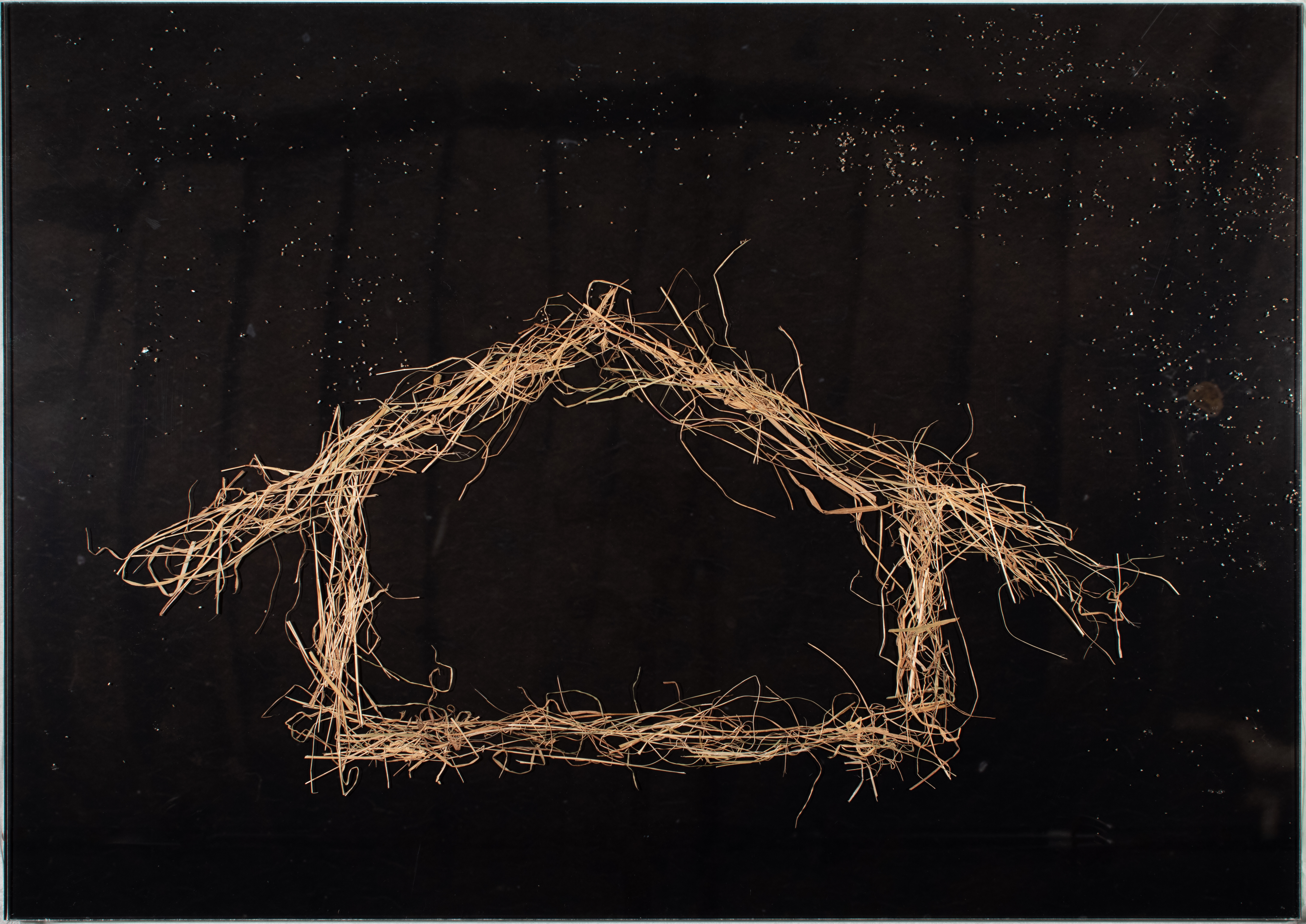 An artwork by George Watson featuring a whare or house form created in straw on a black background. 