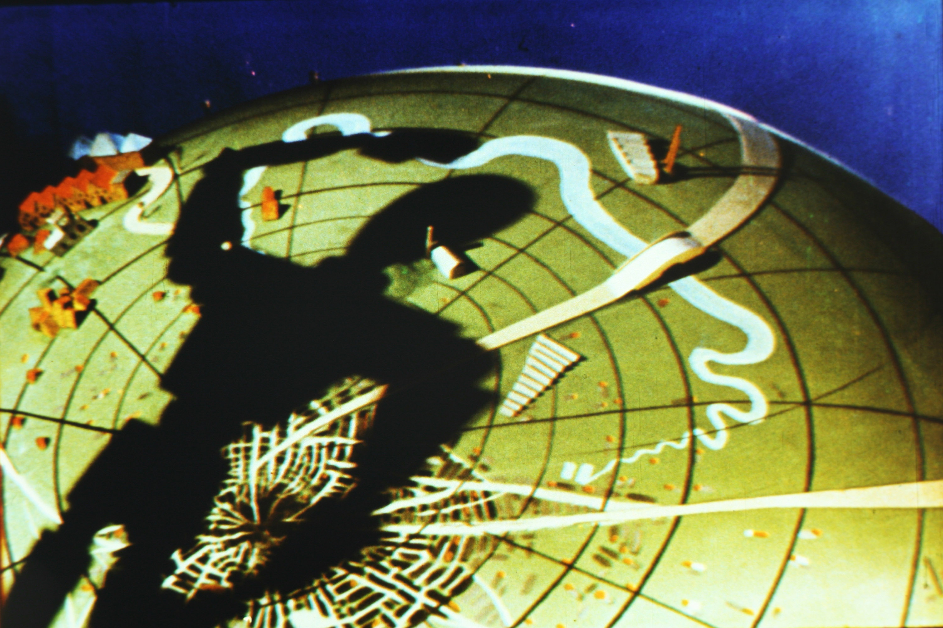 A film still from Len Lye's 1936 film birth of a robot, which shows the shadow of a robot falling over the globe.